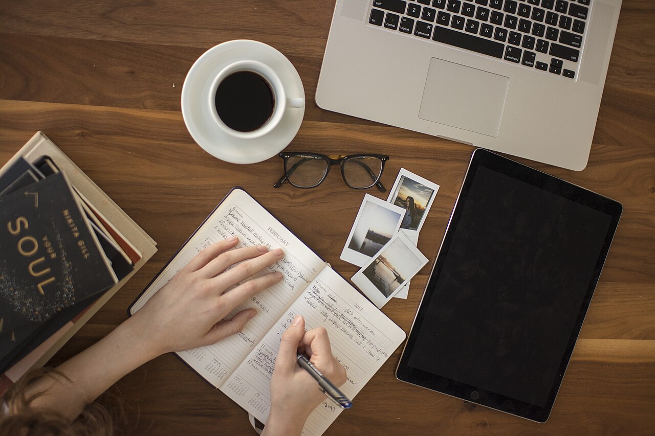 Persona escribiendo en una libreta de planificación sobre una mesa de madera