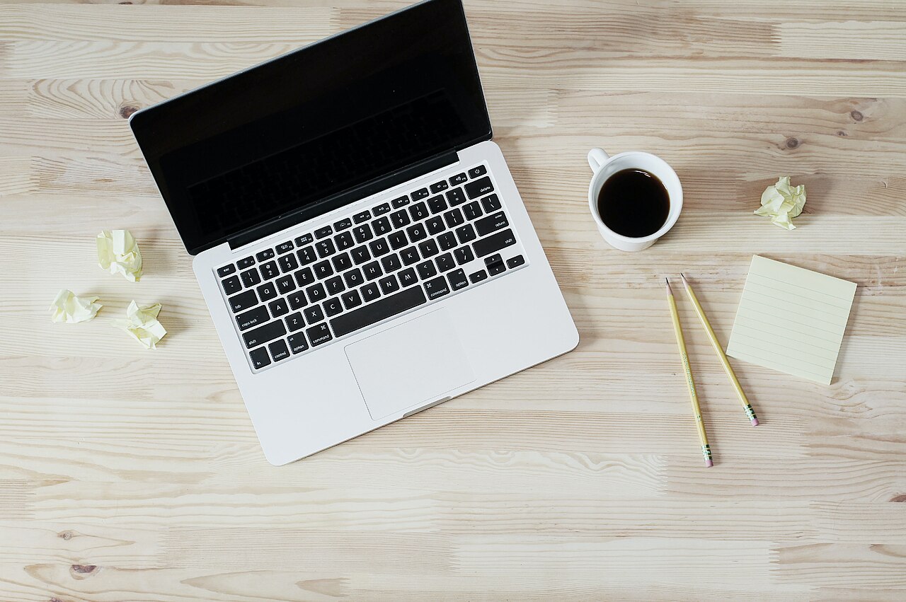Portátil abierto sobre una mesa de madera con cuaderno, notas adhesivas y café